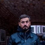Casual portrait of a man wearing a leather jacket in an outdoor urban setting.